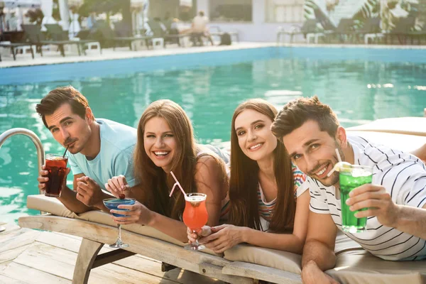 Felices jóvenes amigos con cócteles frescos de verano relajándose cerca de la piscina — Foto de Stock