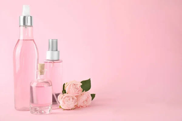 Bouteilles d'huile essentielle et roses sur fond rose. Espace pour le texte — Photo