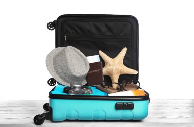 Ahşap masa üzerinde farklı plaj nesneleri ile açık turkuaz bavul, beyaz arka plan