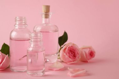 Pembe arka plan üzerinde uçucu yağ ve gül şişeleri