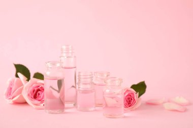 Pembe arka planda uçucu yağ ve gül şişeleri. Metin için alan