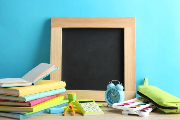 Papelaria escolar diferente e pequeno quadro em branco na mesa perto da parede azul claro. Espaço para texto — Fotografia de Stock