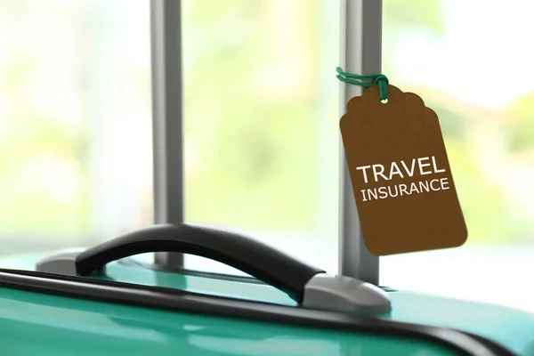 Stylowa walizka z etykietą ubezpieczenia podróżnego na niewyraźne tło, zbliżenie. Miejsce na tekst — Zdjęcie stockowe