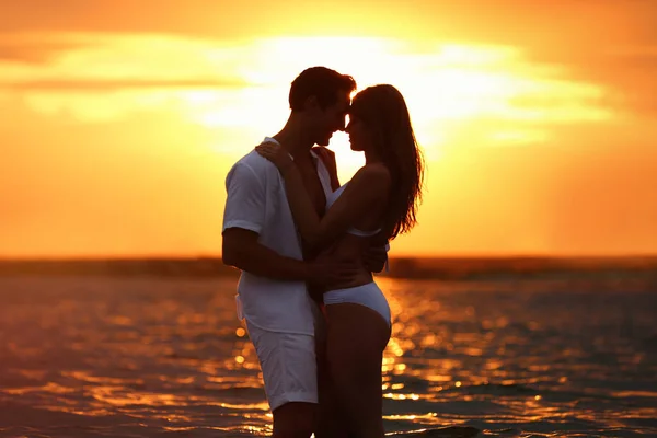 Happy young couple spending time together on sea beach at sunset — Stock Photo, Image