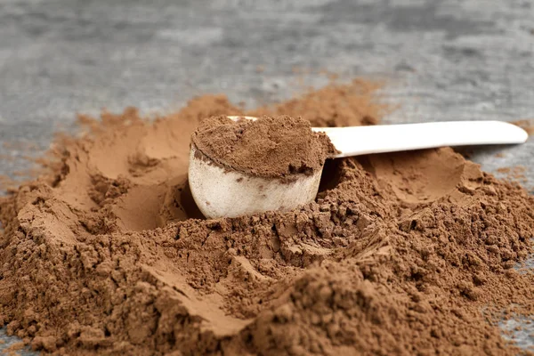 Stapel chocolade proteïne poeder en schep op grijze tafel, close-up — Stockfoto