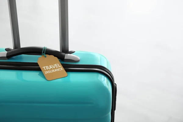 Stylish suitcase with travel insurance label on light background, closeup. Space for text
