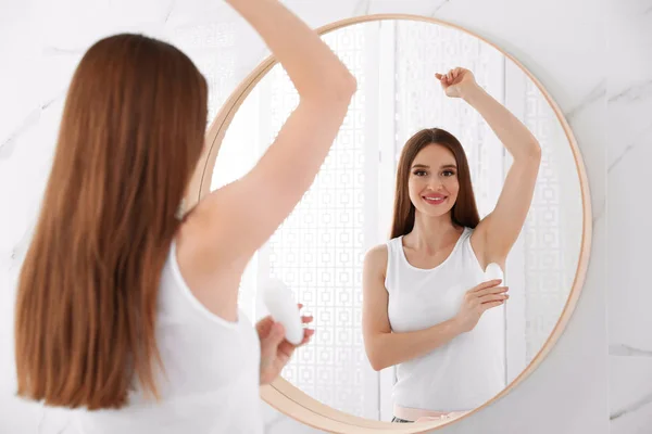 Mooie jonge vrouw die deodorant aanbrengt in de badkamer — Stockfoto