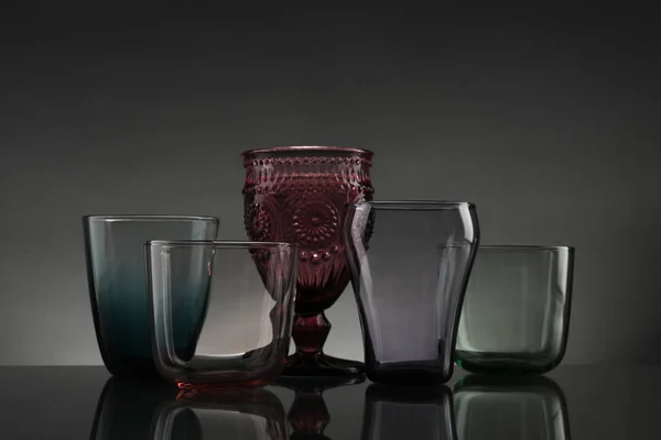 Conjunto de diferentes vidros vazios coloridos na mesa contra fundo cinza — Fotografia de Stock
