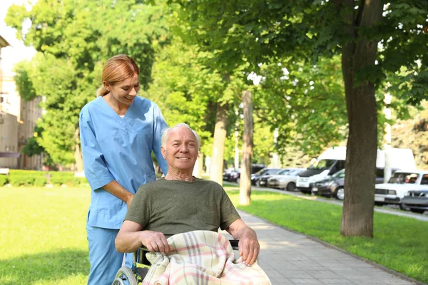 Szczęśliwy pielęgniarka pomoc starszy mężczyzna w Wheelchair w Park — Zdjęcie stockowe