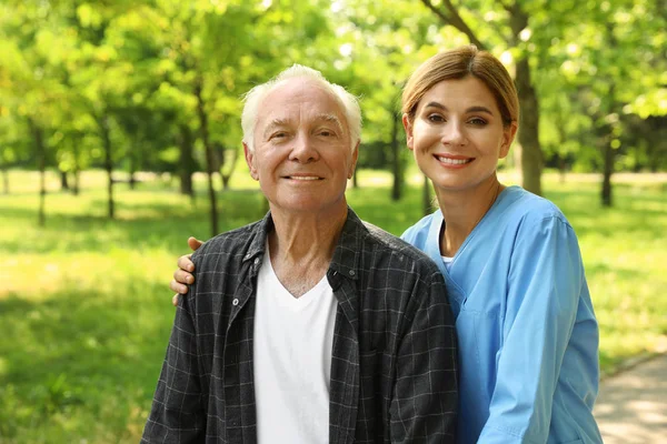 Πορτρέτο του ευτυχισμένο ηλικιωμένο άντρα και νοσοκόμα στο ηλιόλουστο πάρκο. Υποβοήθηση ηλικιωμένων — Φωτογραφία Αρχείου