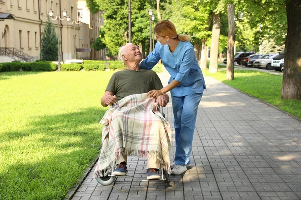 Happy nurse assisting elderly man in wheelchair at park