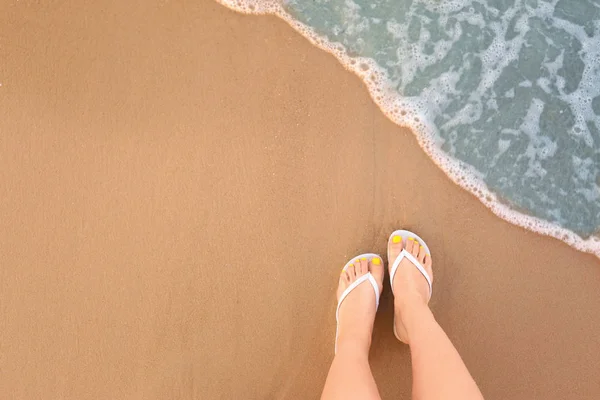 Bovenaanzicht van de vrouw met witte flip flops op zand in de buurt van zee, ruimte voor tekst. Strand accessoires — Stockfoto