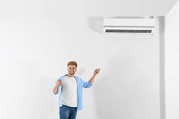 Young man operating air conditioner with remote control indoors. Space for text