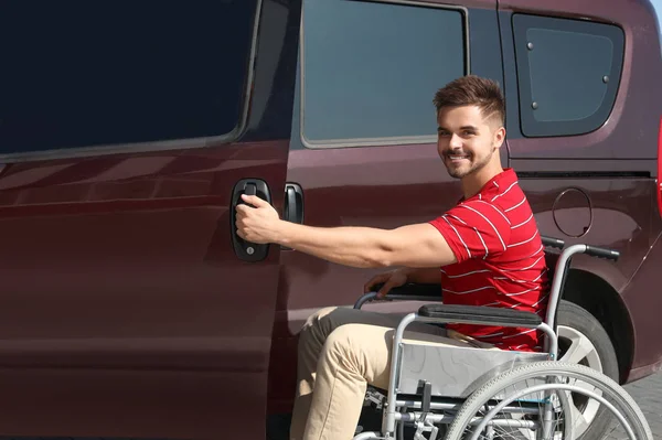 Young man in wheelchair opening door of his van outdoors