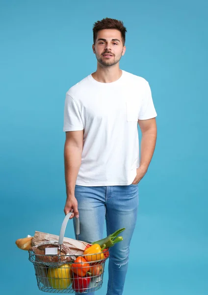 Junger Mann mit Einkaufskorb voller Produkte auf blauem Hintergrund — Stockfoto