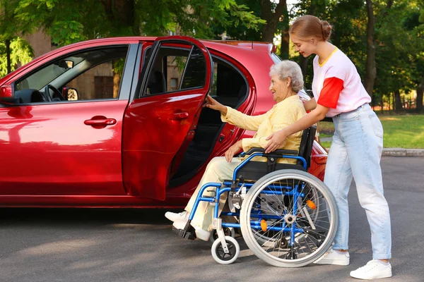 Giovane donna che aiuta la nonna disabile in sedia a rotelle per entrare in auto all'aperto — Foto Stock