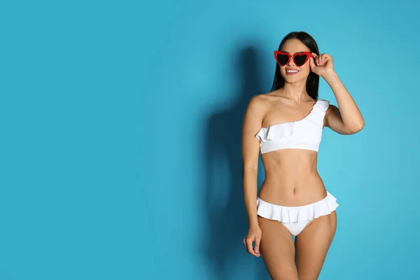 Mooie jonge vrouw in witte bikini met zonnebril op licht blauwe achtergrond. Ruimte voor tekst — Stockfoto