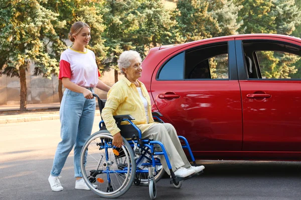 Starsza kobieta w wózku inwalidzkim z wnuczką w pobliżu samochodu na zewnątrz — Zdjęcie stockowe