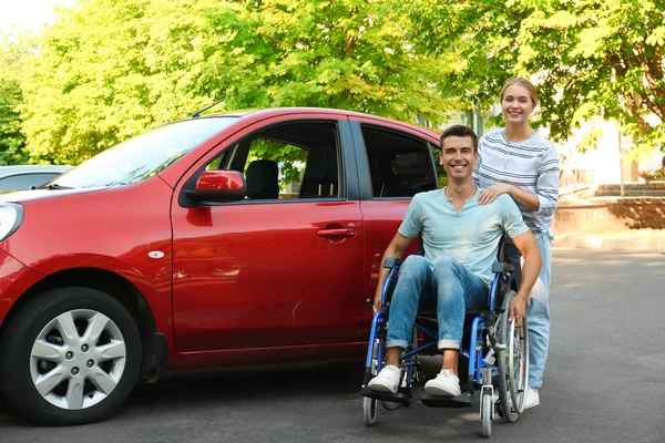 Молодая женщина с инвалидом мужчина в инвалидной коляске возле автомобиля на открытом воздухе — стоковое фото
