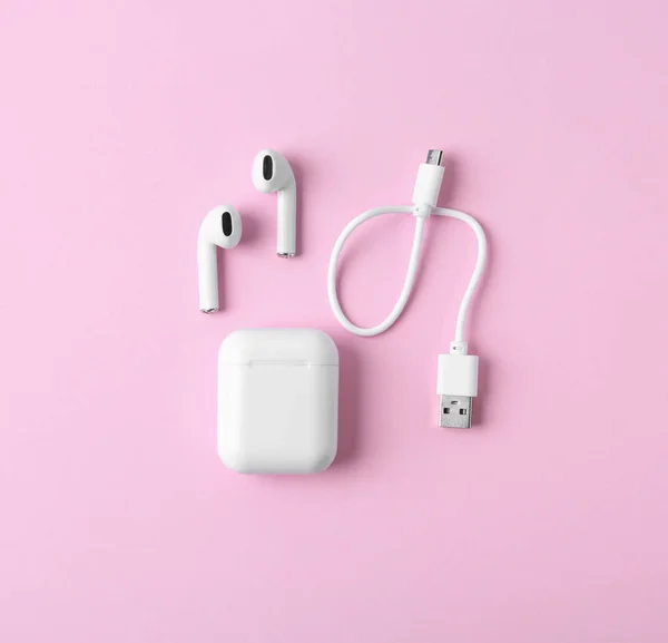 Modern wireless earphones and charging case with cable on pink background, flat lay — Stock Photo, Image