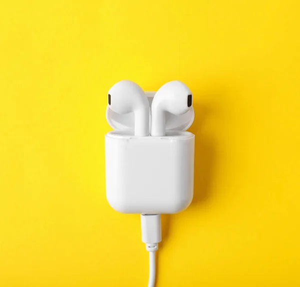 Modern wireless earphones in charging case with cable on yellow background, top view — Stock Photo, Image