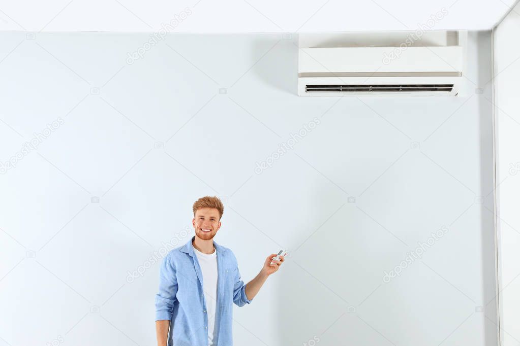 Young man operating air conditioner with remote control indoors. Space for text