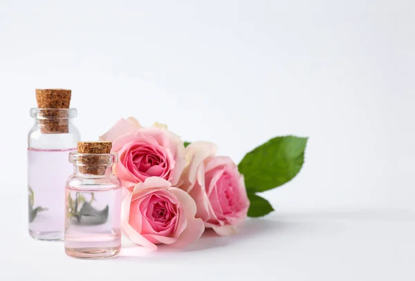 Botellas de aceite esencial y rosas sobre fondo blanco —  Fotos de Stock