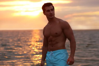 Yakışıklı genç adam gün batımında deniz kenarında sahilde poz