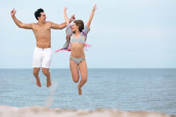 Felice giovane coppia che salta insieme sulla spiaggia di mare. Spazio per testo — Foto Stock