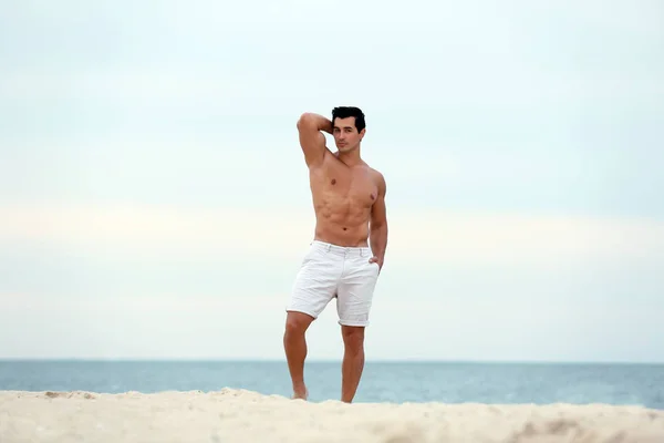 Schöner junger Mann posiert am Strand am Meer — Stockfoto