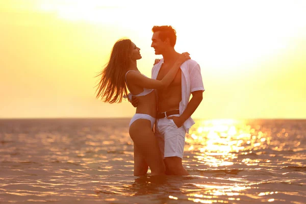 Happy young couple spending time together on sea beach at sunset — Stock Photo, Image