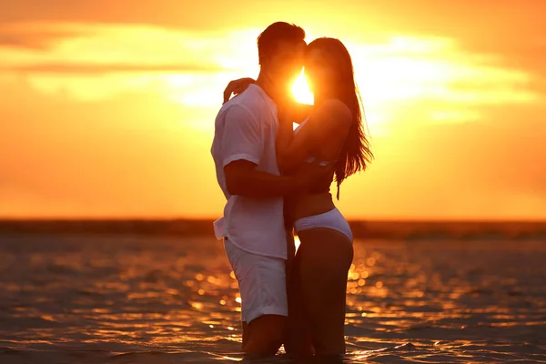 Счастливая молодая пара проводит время вместе на пляже на закате — стоковое фото