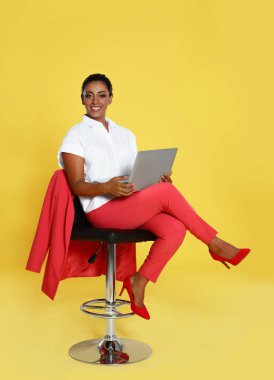 Sarı arka plan karşı sandalyede oturan dizüstü bilgisayar ile Güzel İspanyol iş kadını