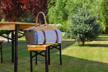 Yeşil bahçede masa yakınında ahşap bankta battaniye ile piknik sepeti. Metin için alan