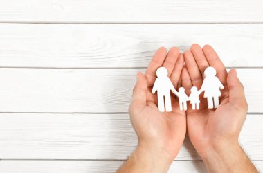 Genç adam beyaz ahşap arka plan karşı elinde aile figürü tutan, üst görünümü. Metin için alan