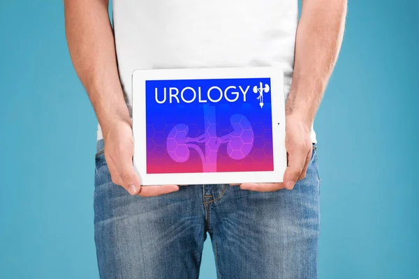 Homme tenant tablette avec mot UROLOGIE à l'écran sur fond bleu, gros plan — Photo