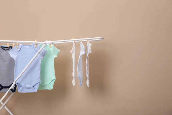 Diferentes onesies bebê bonito pendurado na linha de roupas contra fundo bege, espaço para texto. Dia de lavandaria — Fotografia de Stock
