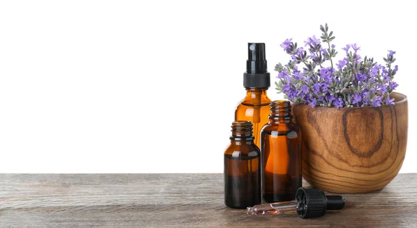 Garrafas de óleo essencial e tigela com flores de lavanda em mesa de madeira contra fundo branco — Fotografia de Stock