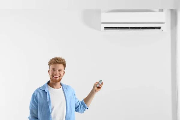 Junger Mann bedient Klimaanlage mit Fernbedienung in Innenräumen. Raum für Text — Stockfoto