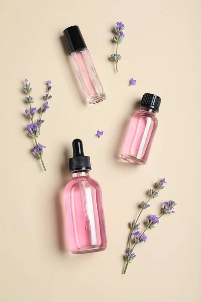 Bottles of essential oil and lavender flowers on beige background, flat lay — Stock Photo, Image