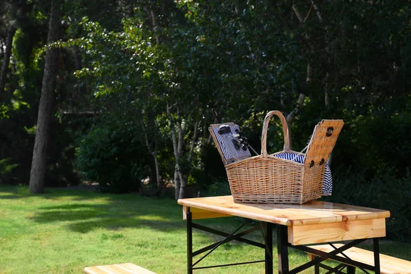 Cesta de picnic abierta sobre mesa de madera en parque verde. Espacio para texto — Foto de Stock