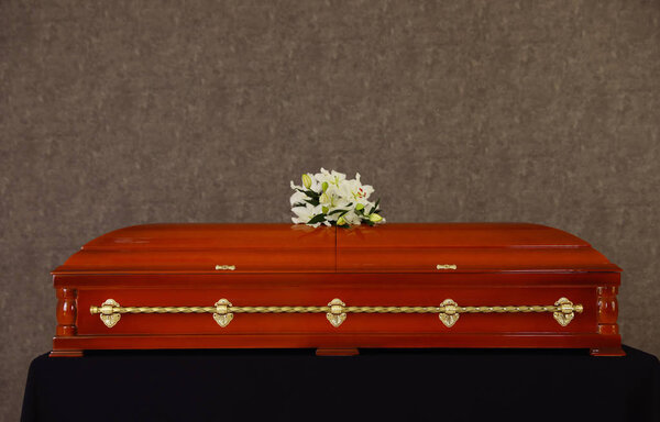 Wooden funeral casket with white lilies at grey wall