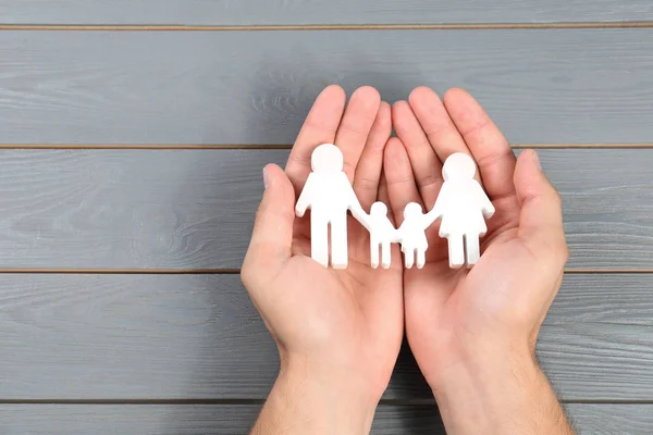 Young man Holding familj figur i händerna mot grå trä bakgrund, uppifrån. Utrymme för text — Stockfoto