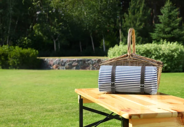 Panier pique-nique avec couverture sur table en bois dans un parc verdoyant — Photo