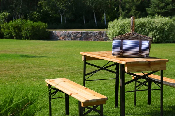 Yeşil parkta ahşap masa üzerinde battaniye ile piknik sepeti