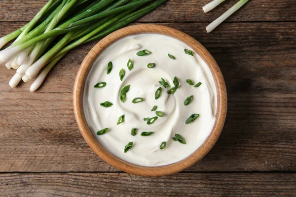 Tigela de creme azedo fresco com cebola verde na mesa de madeira, flat lay — Fotografia de Stock