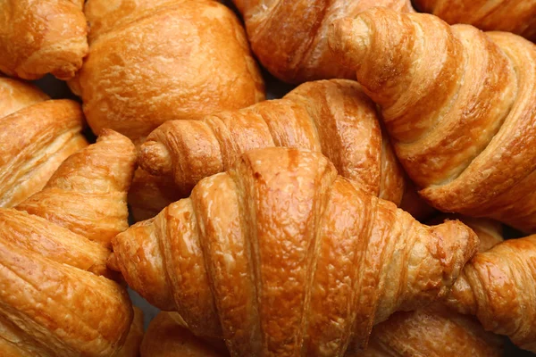 Friss ízletes croissant, mint a háttér, closeup. Francia cukrászsütemény — Stock Fotó