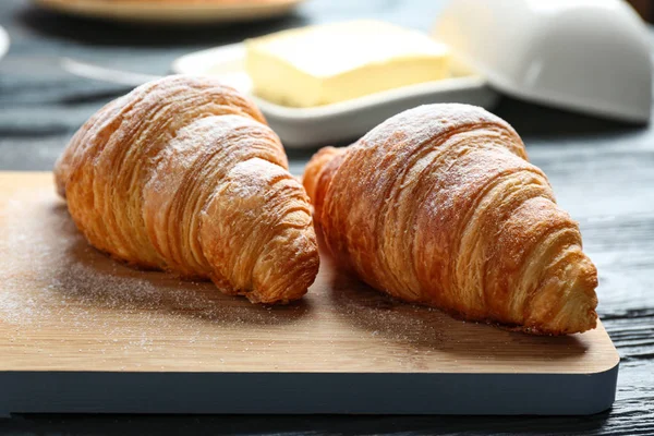 Tablero de madera con sabrosos croissants en la mesa, primer plano. Pastelería francesa — Foto de Stock