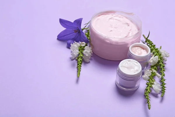 Frascos de crema corporal y flores sobre fondo lila. Espacio para texto — Foto de Stock