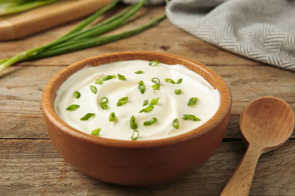 Cuenco de crema agria fresca con cebolla verde y cuchara en la mesa de madera — Foto de Stock